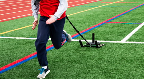 High school runner pulling a sled with weight on green turf field