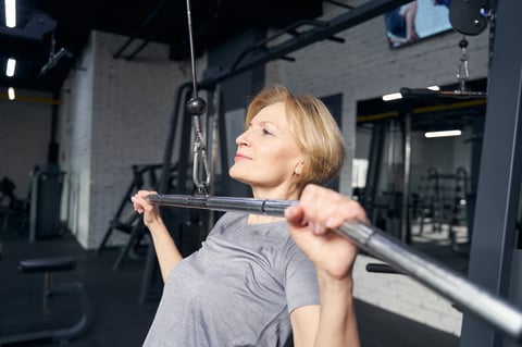 Blonde female person holding metal bar exercising with gym equipment