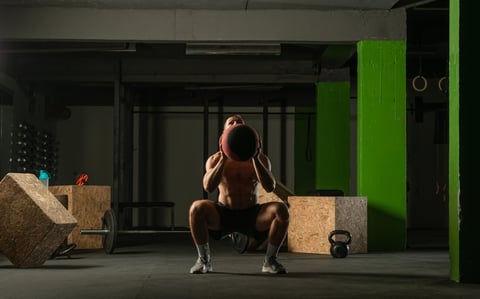 Fit man throwing medicine ball doing ball slam against gym floor or shoulder press exercise