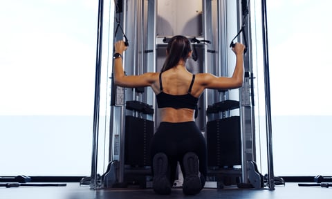 Sporty woman exercising on multistation at gym for arm and shoulders muscles