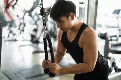 Focused man in a black tank top performs a tricep pushdown exercise using a cable machine
