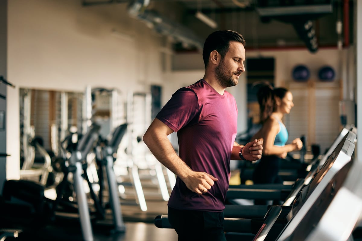 Side profile of a male and female running on a treadmill at the gym