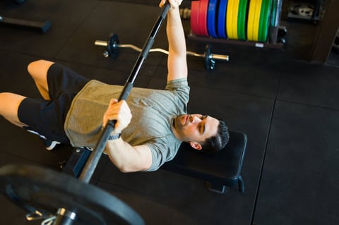 Determined male athlete lifting a barbell while doing bench press exercises