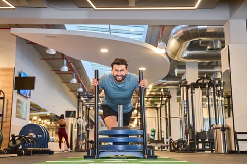 Energetic man pushing a weighted sled on turf in a contemporary gym