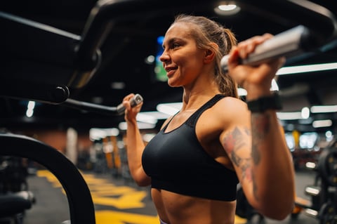Determined young adult woman lifting weights, focused on her fitness goals in a modern gym