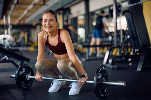 Happy female athlete exercising with barbell in a gym and looking at camera