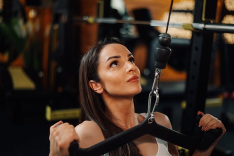 Young woman using a lat pull-down machine, strengthening her back muscles during an intense workout session