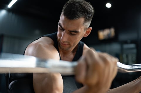 Muscular athletic young man doing biceps curls exercising with EZ curl bar at the gym