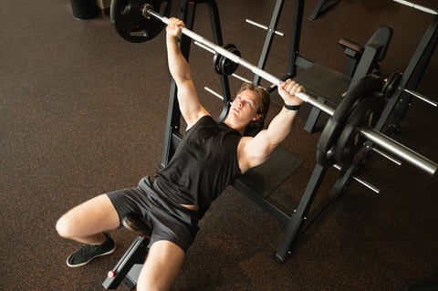 Young caucasian man exercising with barbell at fitness center