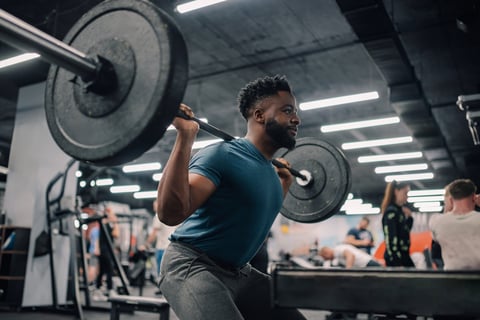 Muscular athlete doing squats with barbell in gym