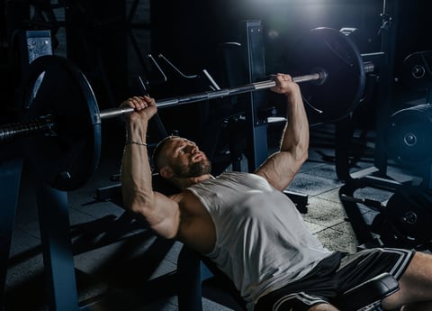 Muscular man training with weights pumping up muscles workout in dark gym