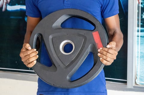 Hand gripping black rubber coated weight plate with red markings