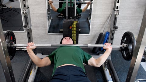 Young Asian man doing bench press training in a sports gym
