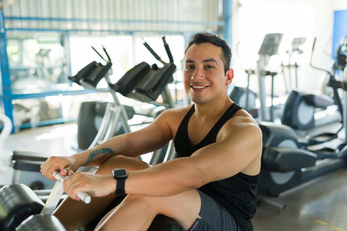 Hombre joven sonriendo a la cámara mientras se ejercita en máquina de remo
