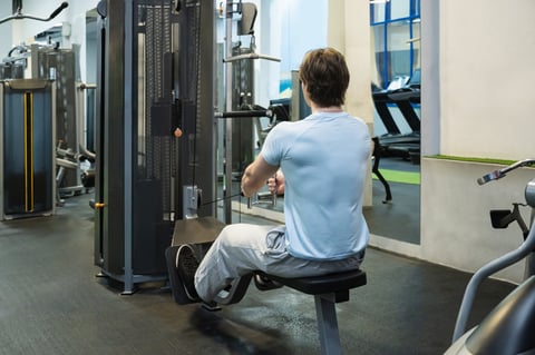 Sporty young man exercising on low rowing machine at gym