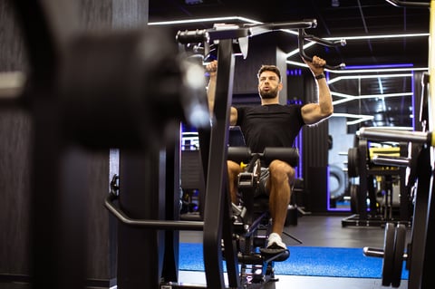 Man engaged in a strength training session using a lat pulldown machine in a well-equipped gym