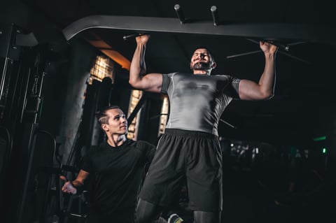 Male bodybuilder performing lat pulldown with trainer in gym
