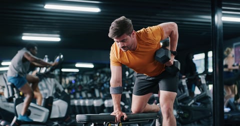 Fit man training with dumbbell row in gym for muscle development
