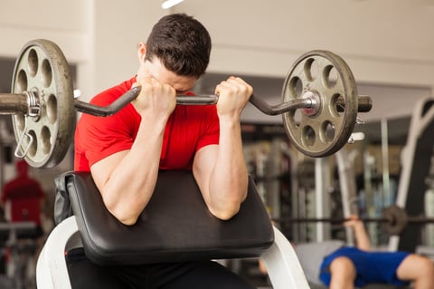 Young athletic man lifting a barbell on a preacher bench at the gym