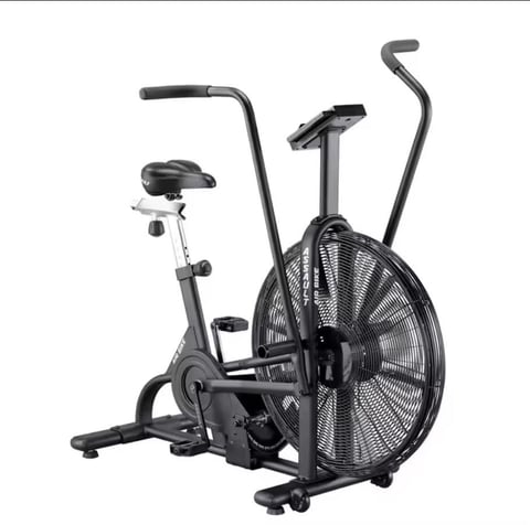 Black stationary exercise bike with large fan wheel and dual handles against white background