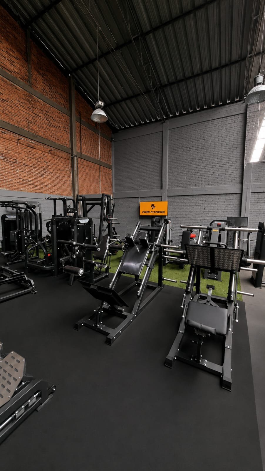Modern indoor fitness studio with stationary bikes and exercise equipment on dark flooring, exposed brick wall, and metal ceiling