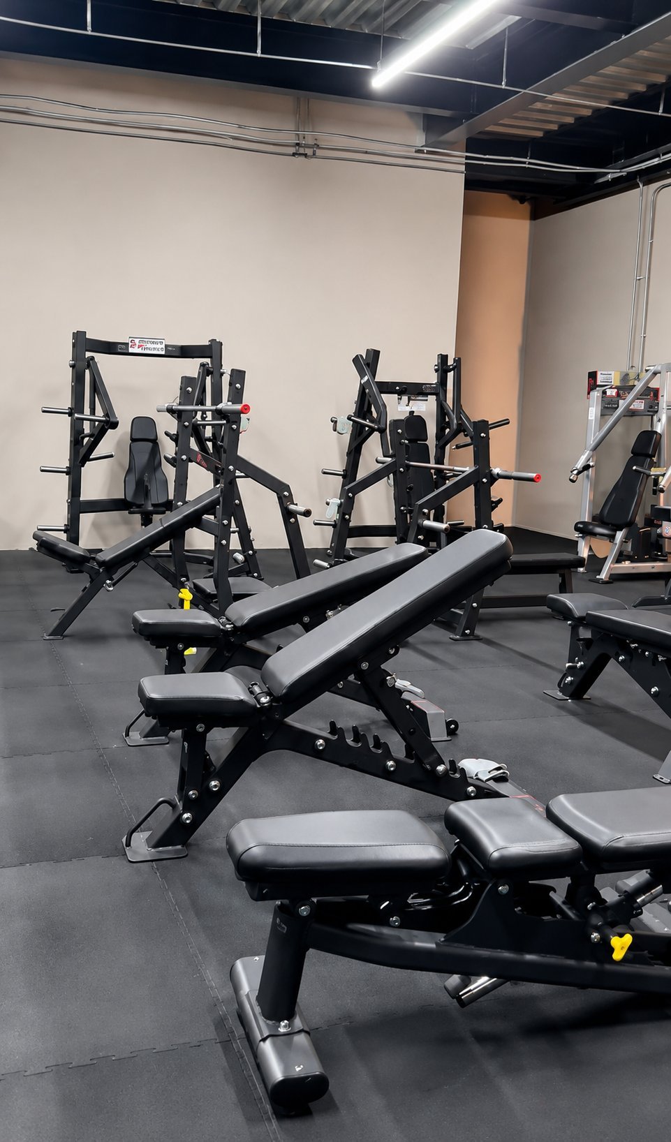 Modern gym interior with black weight benches and cardio machines on dark flooring under industrial ceiling lights